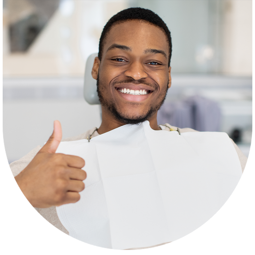 The image shows a man sitting in a dental chair with his mouth open, smiling broadly, and giving a thumbs-up gesture. He appears to be happy and satisfied with his dental care experience.