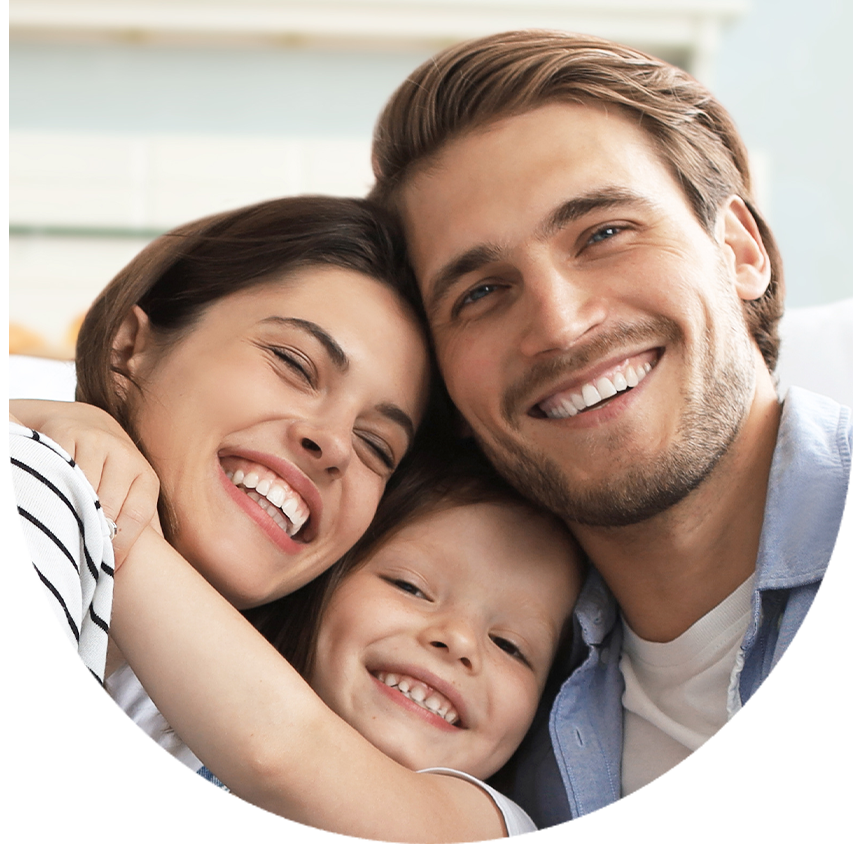 The image shows a family of four, consisting of an adult couple and their two children, hugging each other with smiles on their faces.